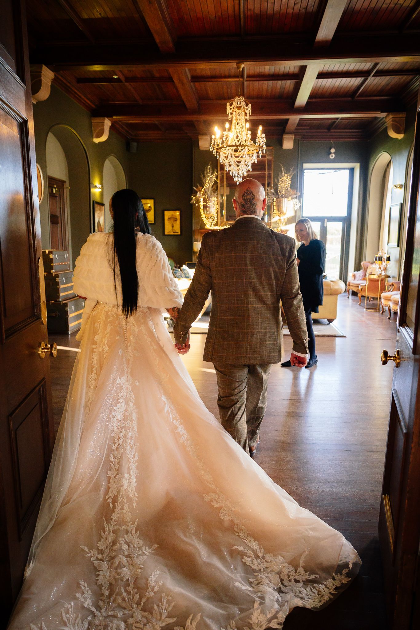 Wedding dress train trailing beautifully across hardwood floor in elegant venue with chandeliers.