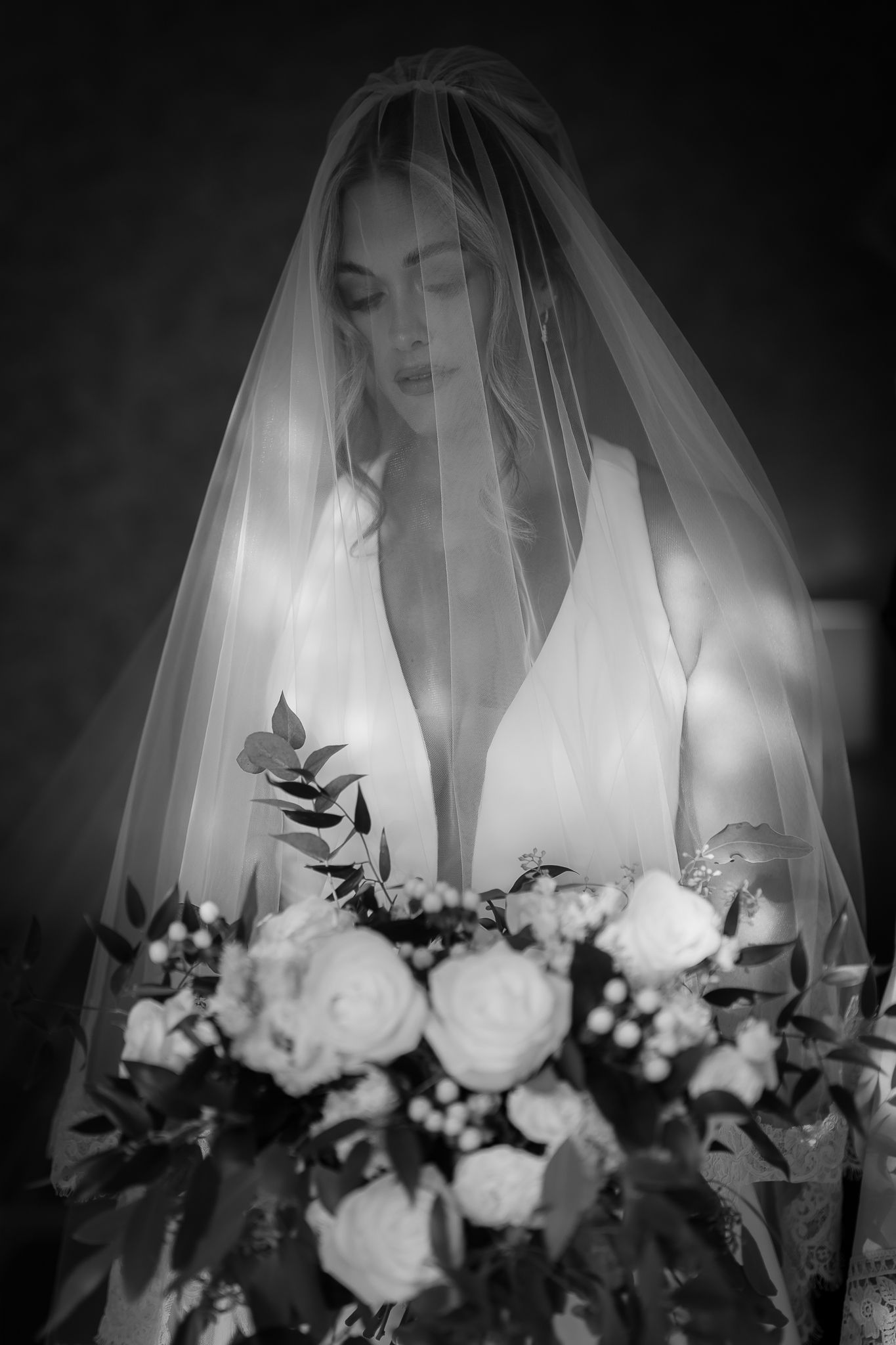 Elegant black and white bridal portrait with white roses and flowing veil.