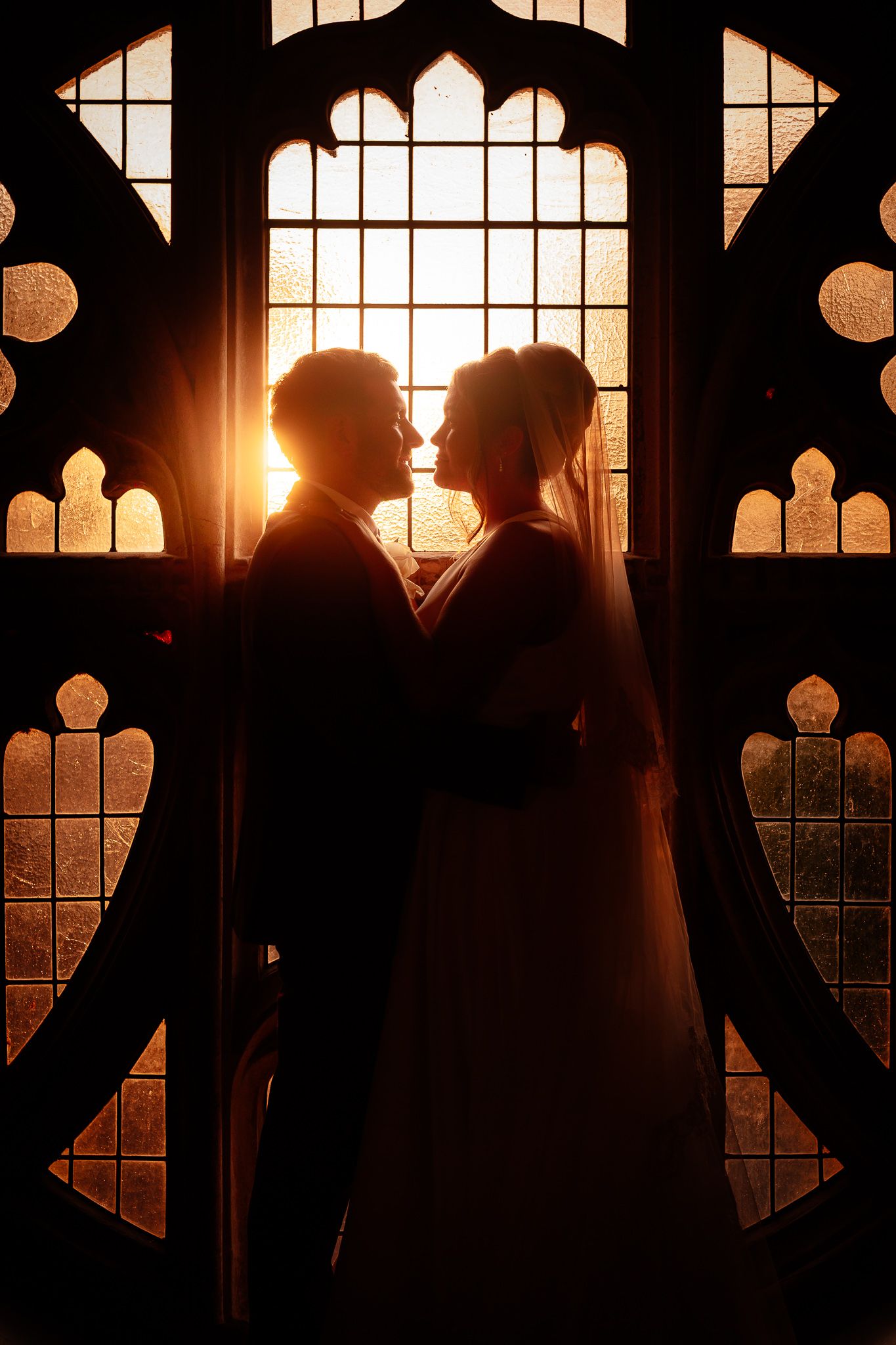 A romantic silhouette against a gothic church window at sunset creates a dramatic wedding portrait.