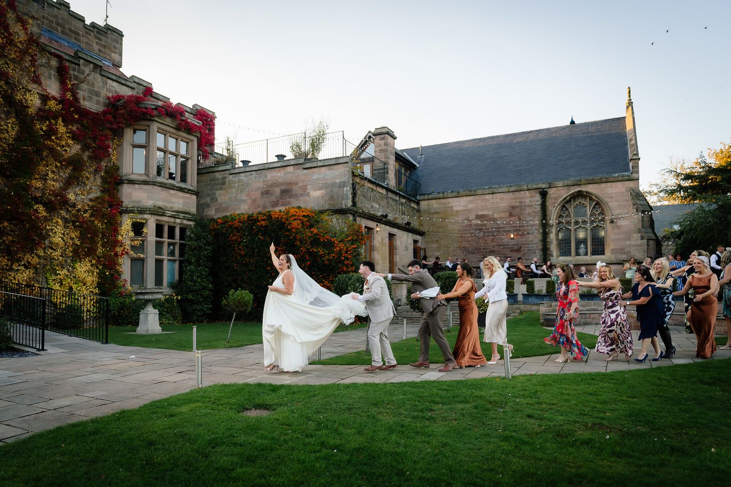 Wedding party playfully tosses the bride's dress on a grand estate lawn.