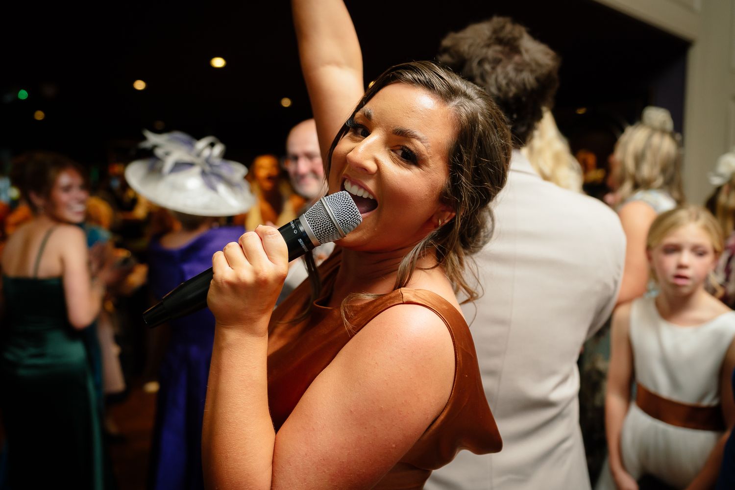 Wedding guest sings enthusiastically into microphone during reception celebration.