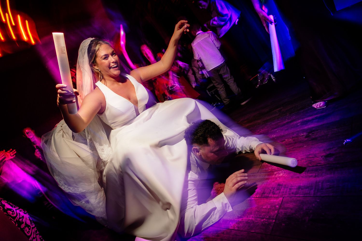 Energetic dancing and celebration at a wedding reception with colorful lighting effects.