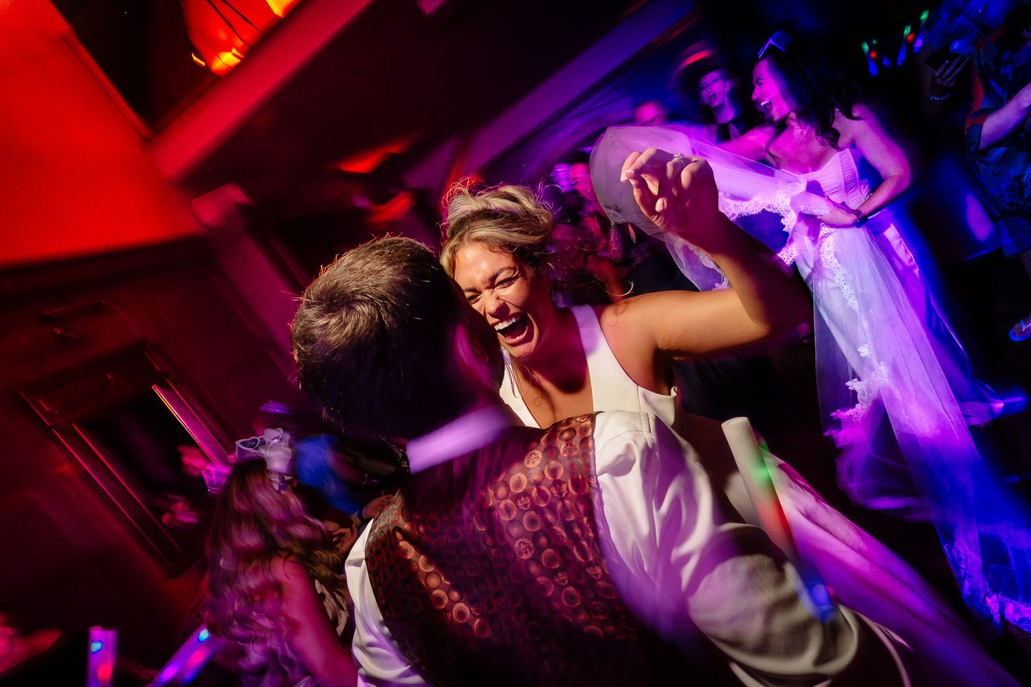 Wedding party dancing under dramatic red and purple lighting at a lively reception.