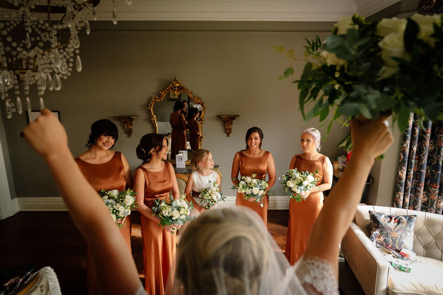 Wedding party holding bouquets aloft in celebration against neutral backdrop.
