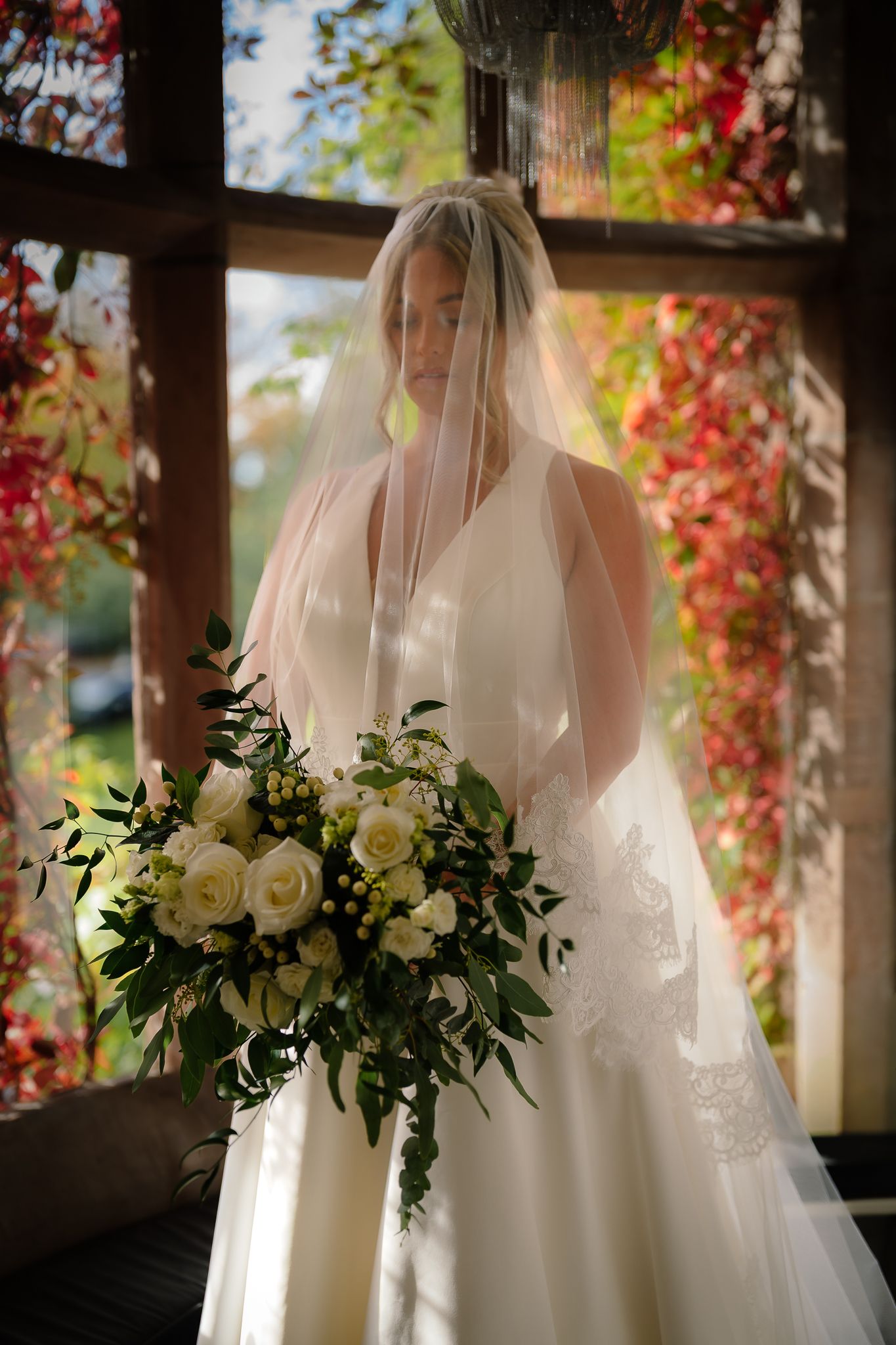 Bridal portrait in natural light with white roses and autumn foliage in background.