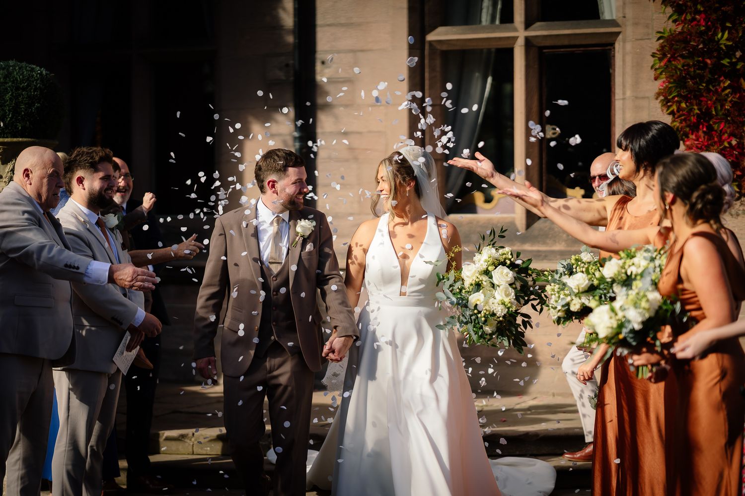 Wedding celebration with guests throwing confetti outside a building at sunset.