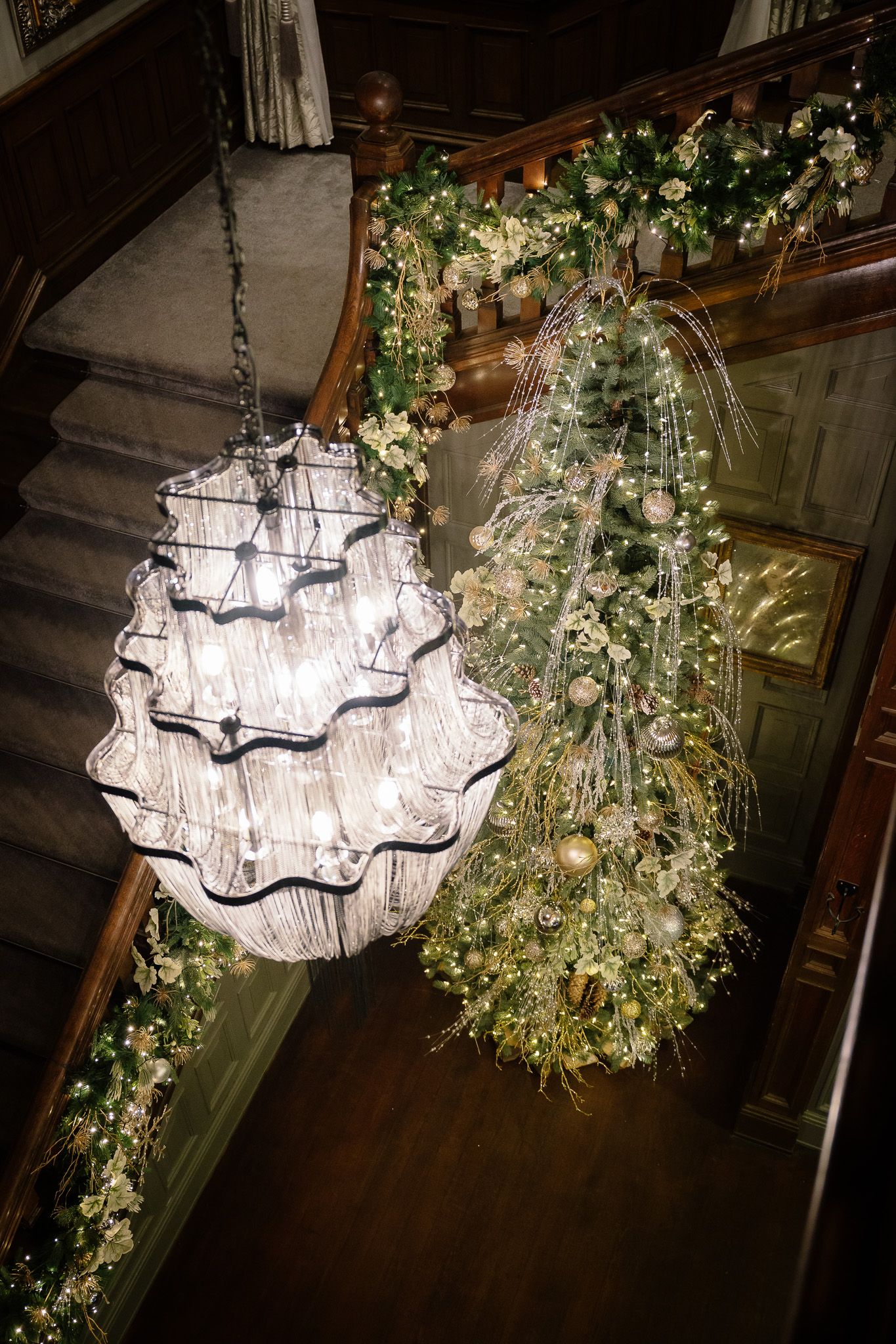 Crystal chandeliers adorned with cascading greenery and floral arrangements create an enchanting ceiling display. Ellingham Hall