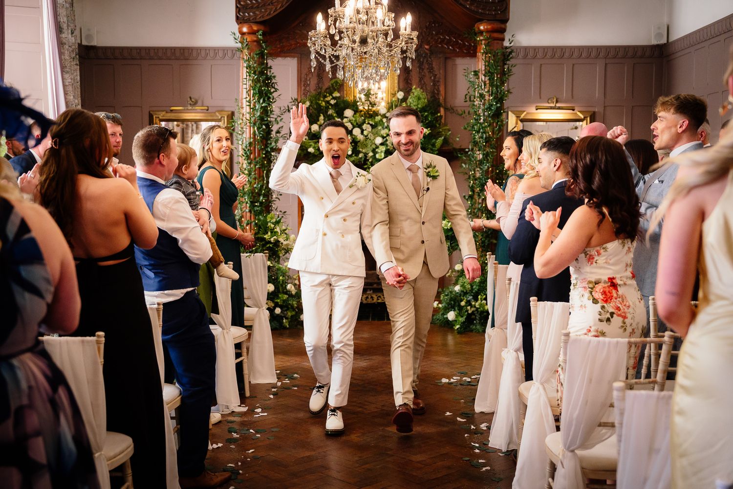 Wedding guests dancing and celebrating on a dance floor under elegant chandeliers.