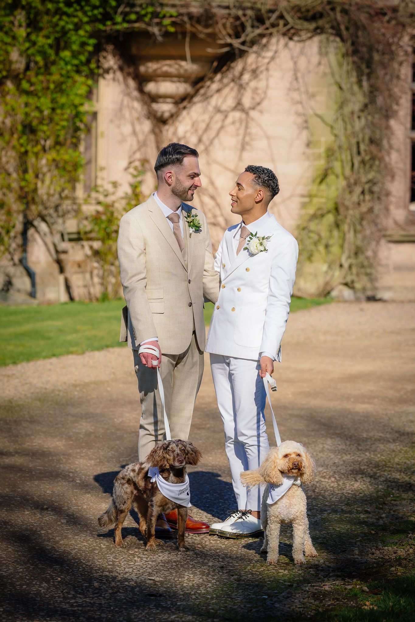 Two people walking dogs together in a garden setting wearing light colored clothing.
