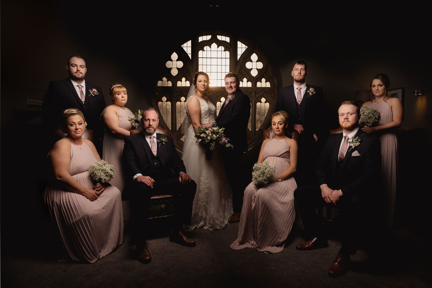 Dramatic low-light portrait of wedding party members in formal attire against dark background. Ellingham Hall