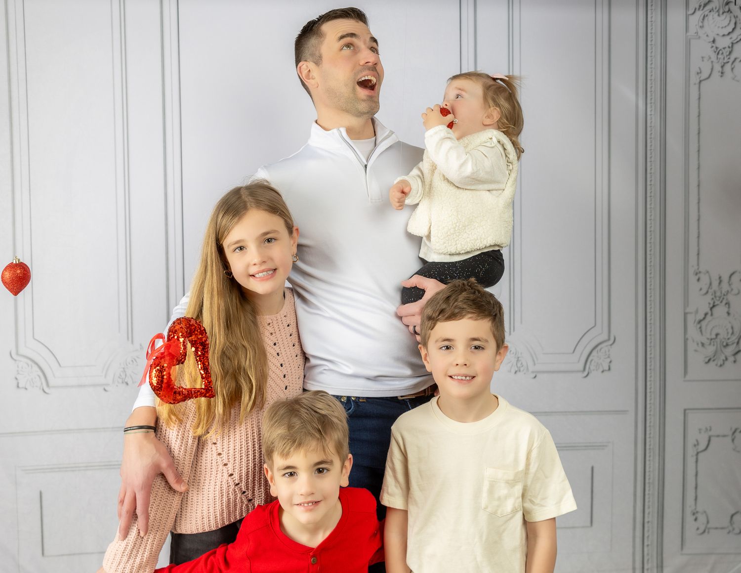 A joyful family wearing red and white outfits poses together against a white backdrop for a holiday portrait.