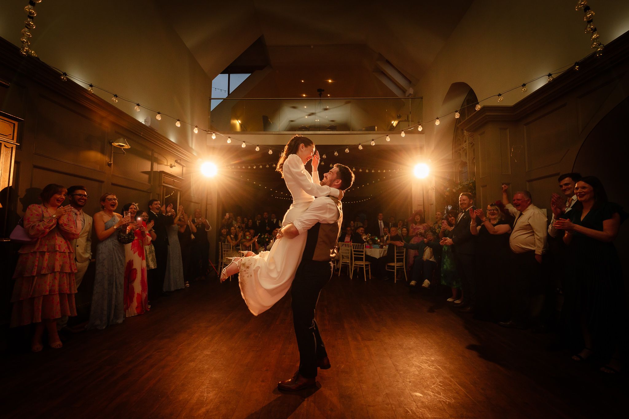 Wide angle shot of a wedding reception dance floor with string lights creating a warm ambiance. Ellingham Hall