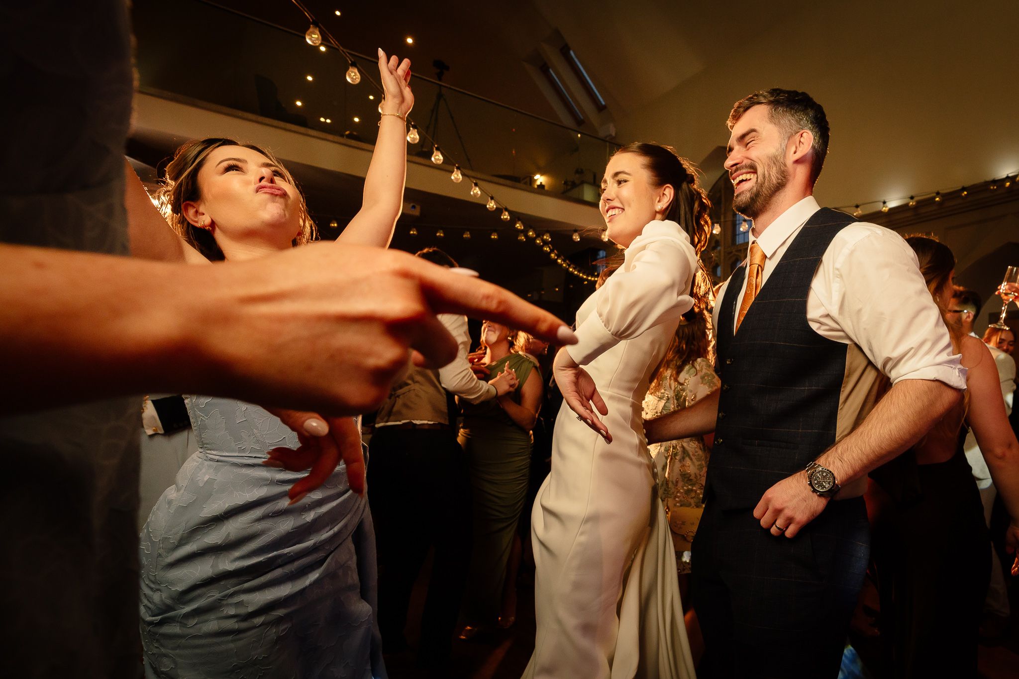 Warm-toned wedding reception photo showing guests dancing in ambient lighting. Ellingham Hall
