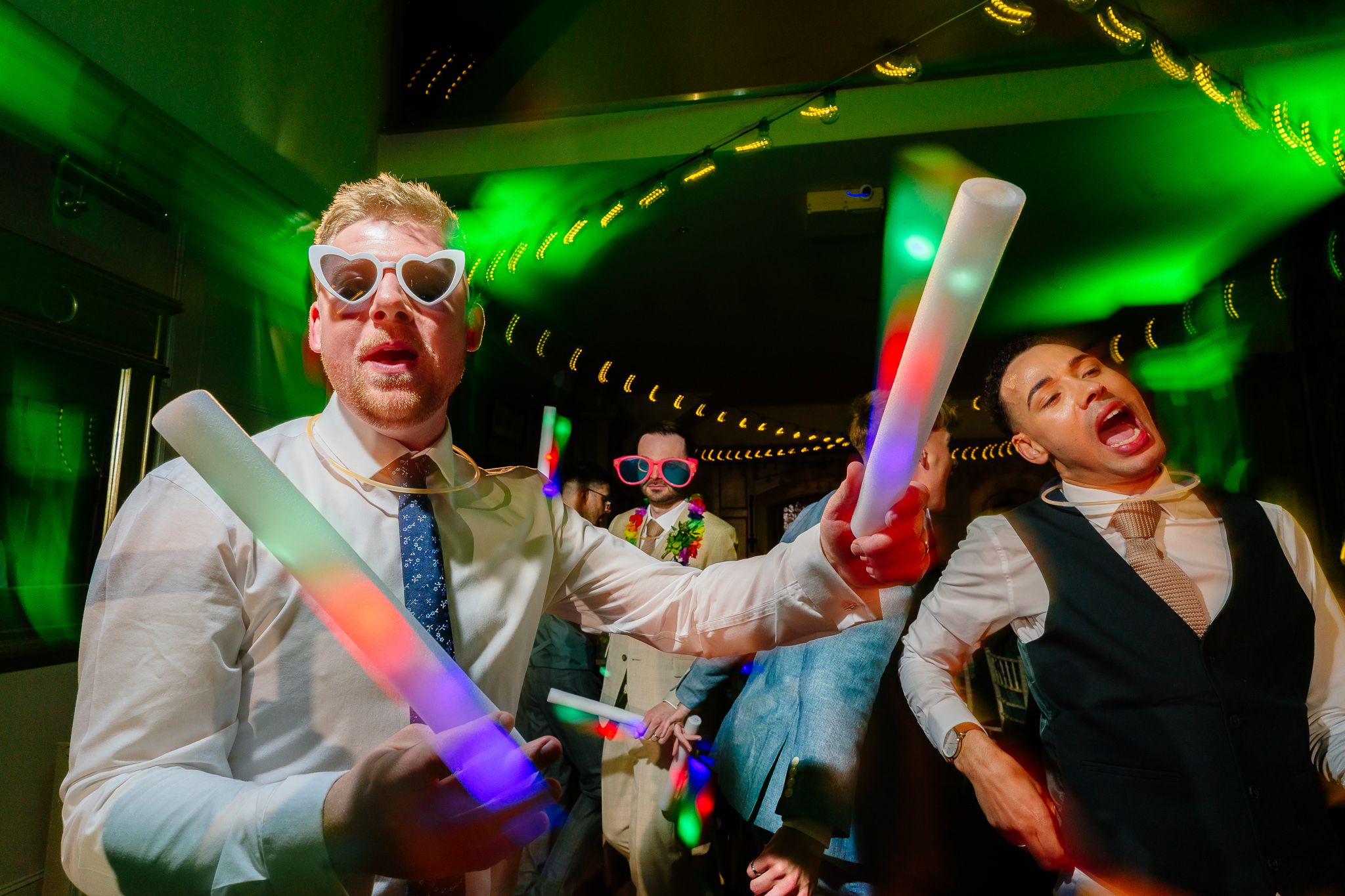 Energetic party scene with green lighting and glow sticks creating a vibrant atmosphere. Ellingham Hall