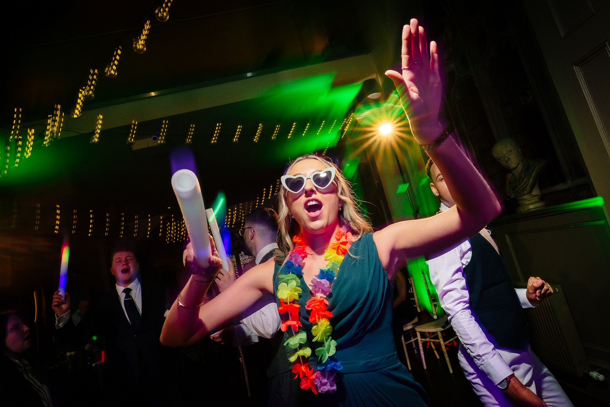 Wedding reception dance floor illuminated with vibrant green and pink lighting creating an energetic party atmosphere. Ellingham Hall