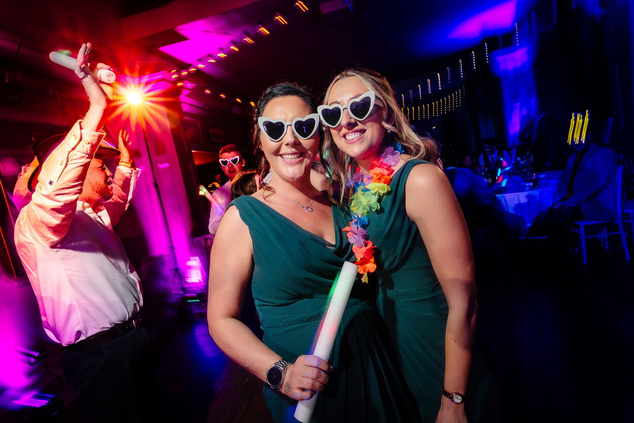 Colorful purple and blue lighting illuminates a lively dance floor at a wedding reception. Ellingham Hall
