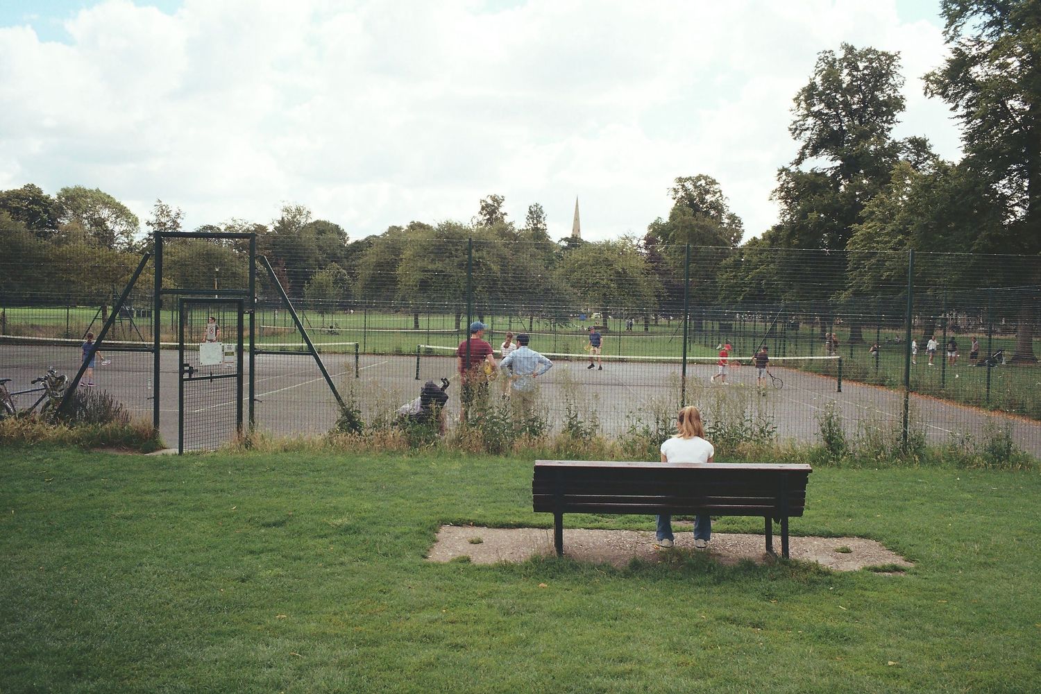 Empty playground equipment and swings stand in a grassy field on a sunny day.