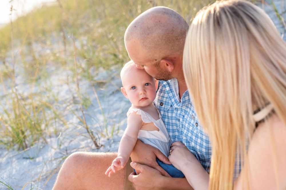 A tender family moment captured at the beach during golden hour with soft natural lighting and coastal vegetation.