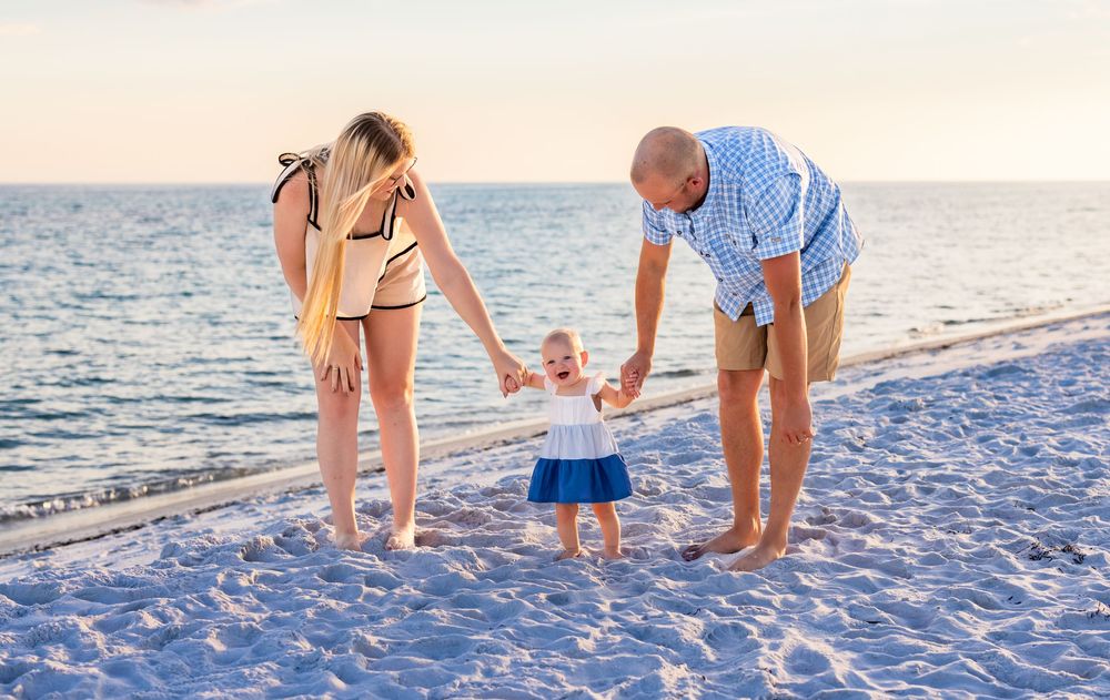 Family members walk together on a white sandy beach at sunset collecting seashells along the shoreline.
