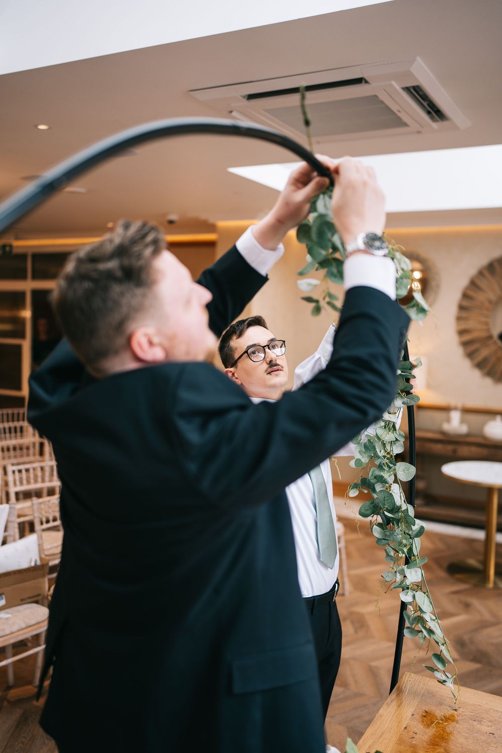 Groomsmen decorate at an indoor wedding reception venue.