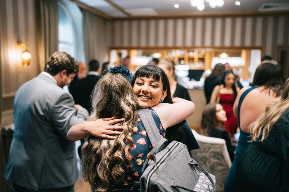 Wedding guests share joyful moments and embraces during an indoor reception celebration.