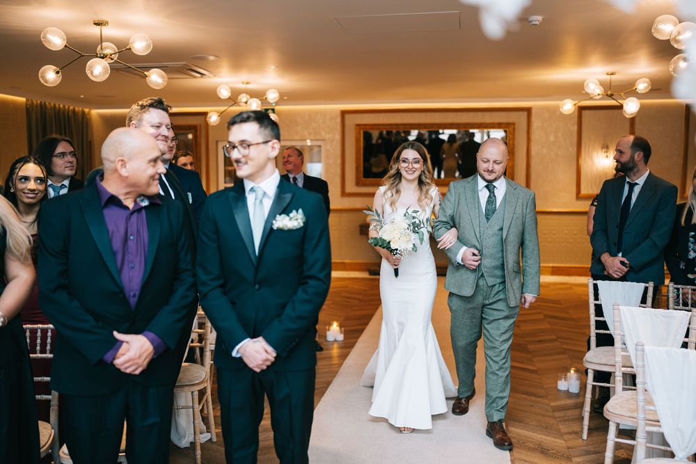 A wedding party walks and mingles in an elegant ballroom with warm lighting and chandelier fixtures.
