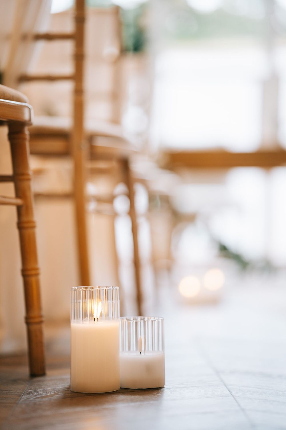 White pillar candles create an elegant atmosphere on wooden tables at a wedding reception.