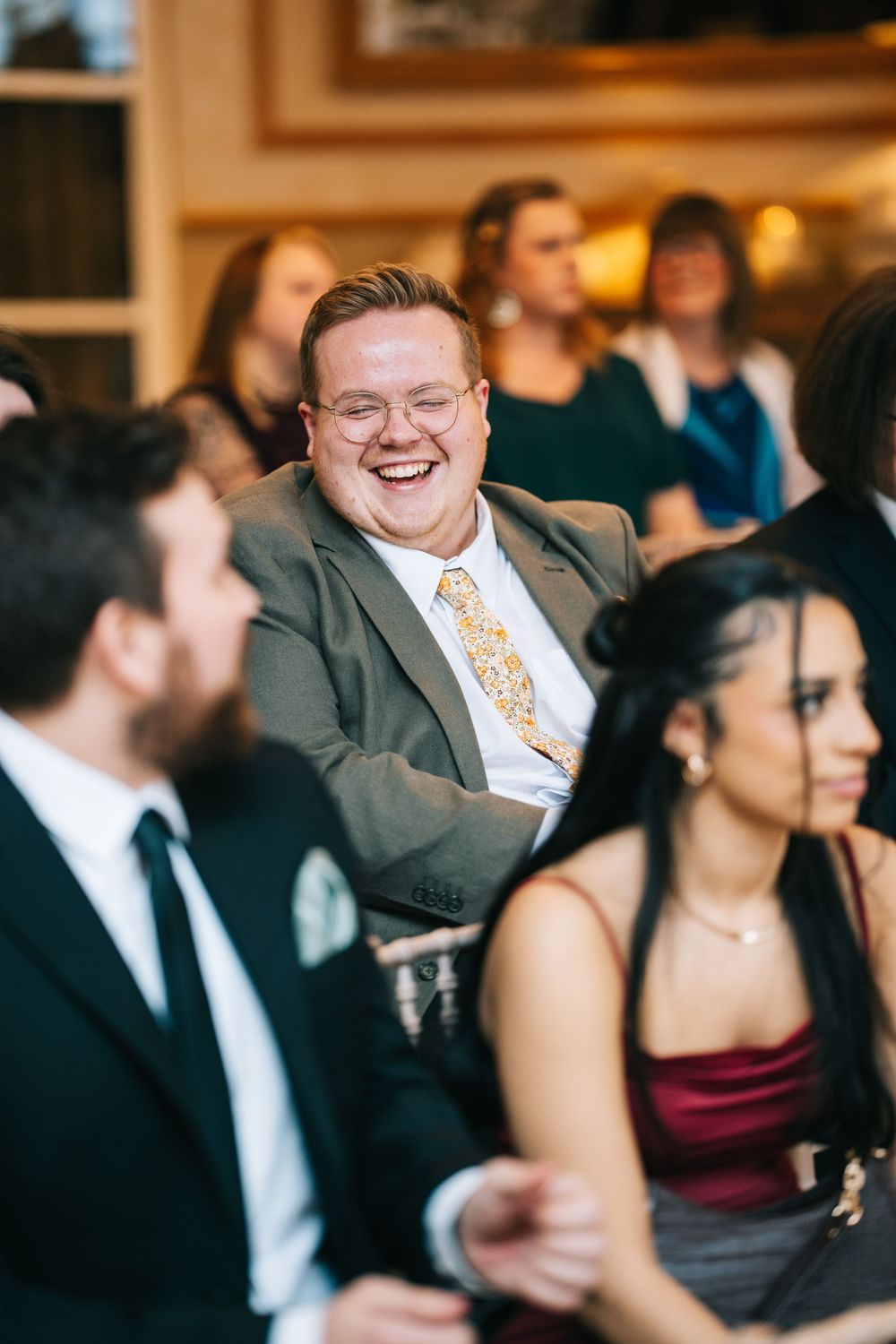 Wedding guests share joyful laughter during a candid moment at an indoor reception venue.