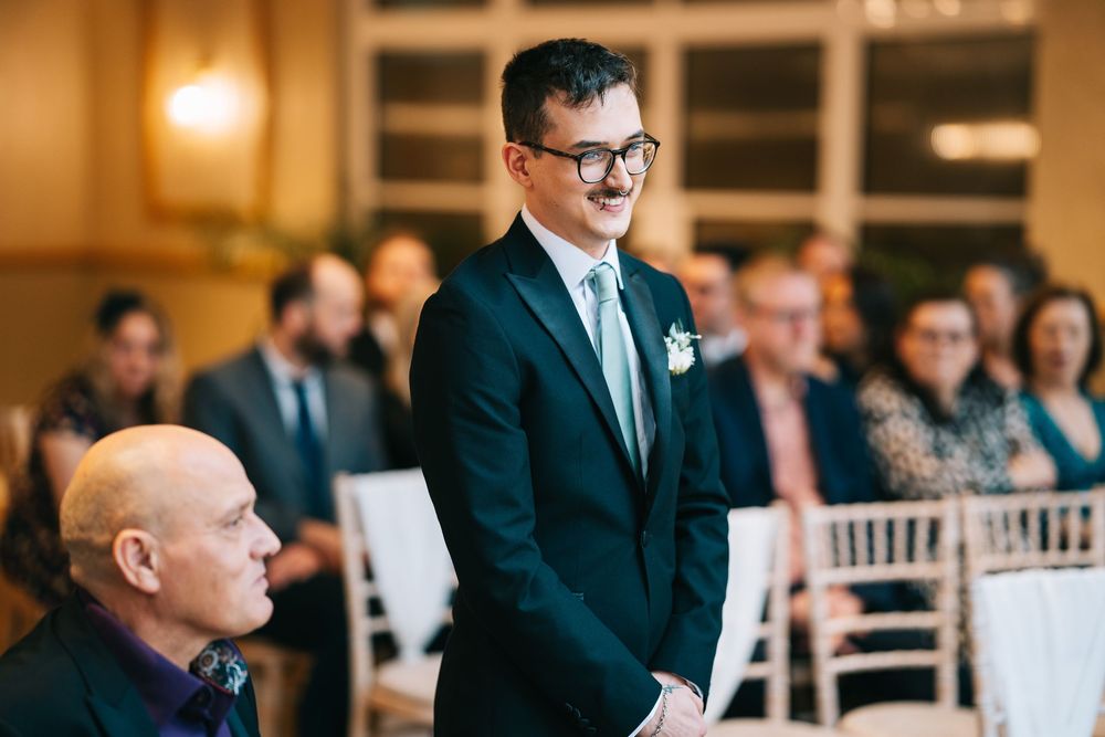 Guests seated in formal attire watch attentively during an indoor wedding ceremony.