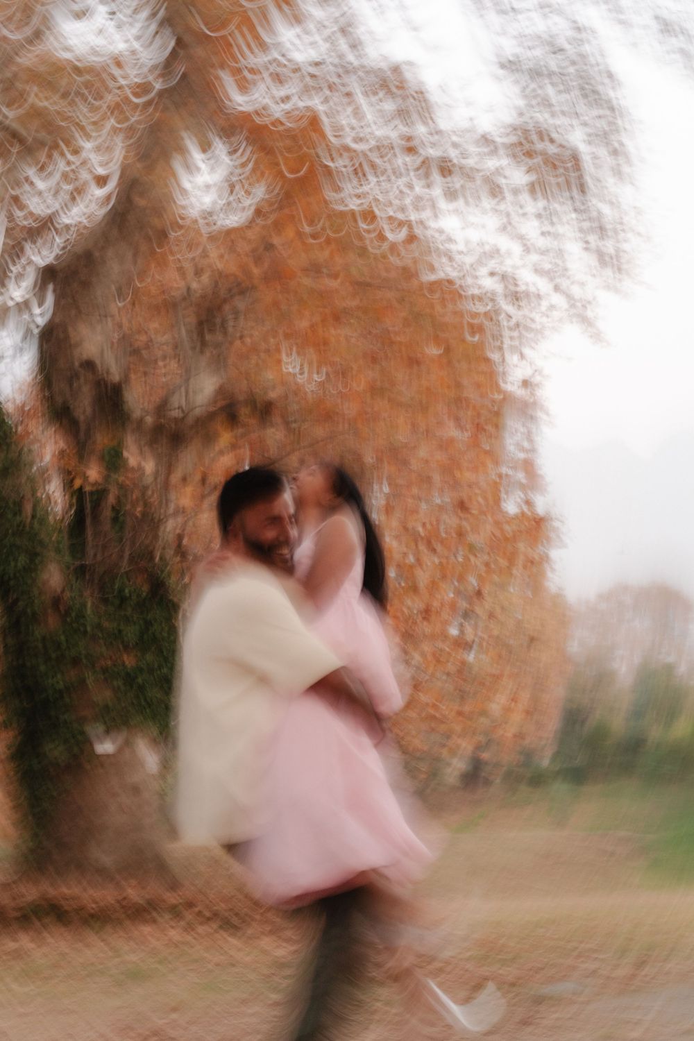 Artistic motion blur photo of a couple dancing in a romantic autumn setting with orange foliage in the background.