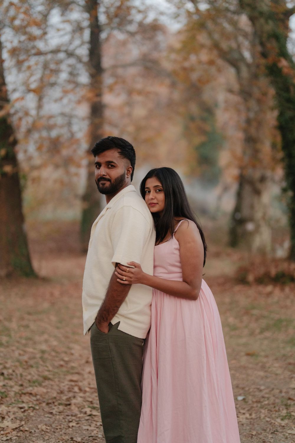 A couple embraces in a romantic autumn setting with fallen leaves and warm lighting.