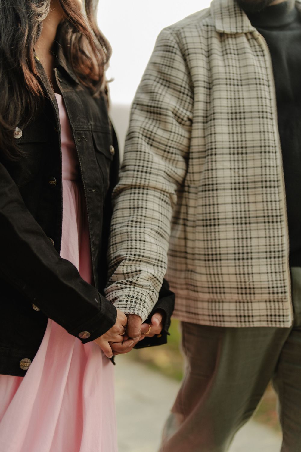 Close-up of a couple holding hands, with one wearing a plaid jacket and the other in a pink dress.