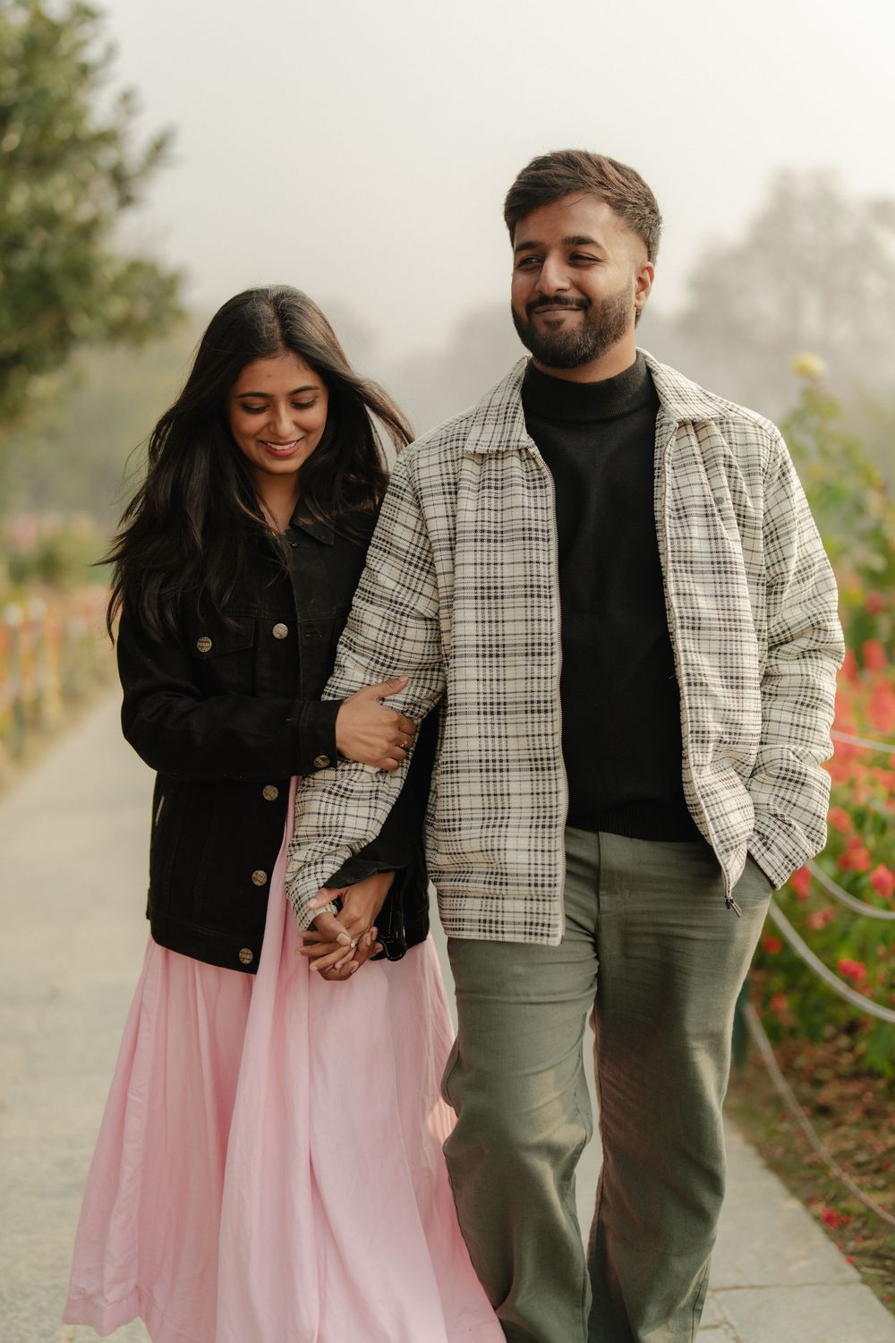 A couple shares joyful moments together in a garden path wearing coordinated outfits of black, pink and plaid.