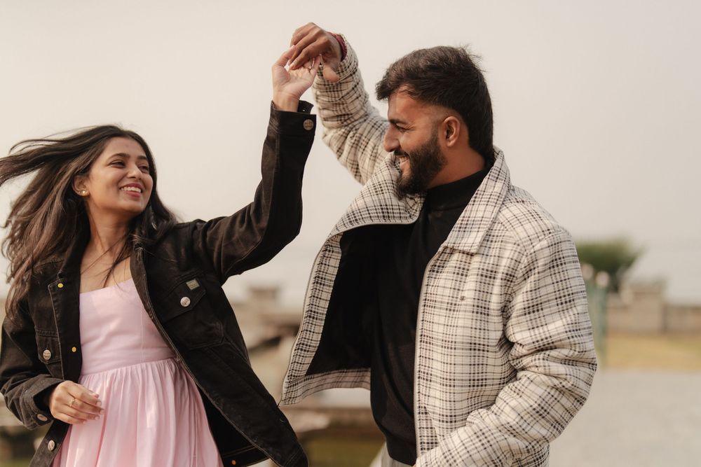 A couple in autumn attire dances playfully together in an outdoor setting during golden hour.