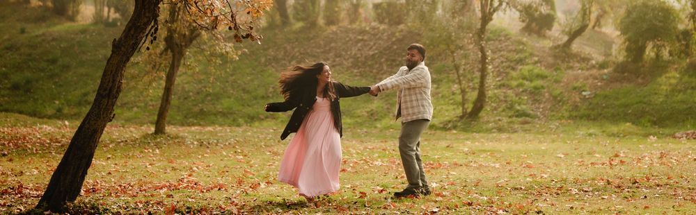 Two people share a romantic dance in a grassy field with trees and warm sunlight in the background.