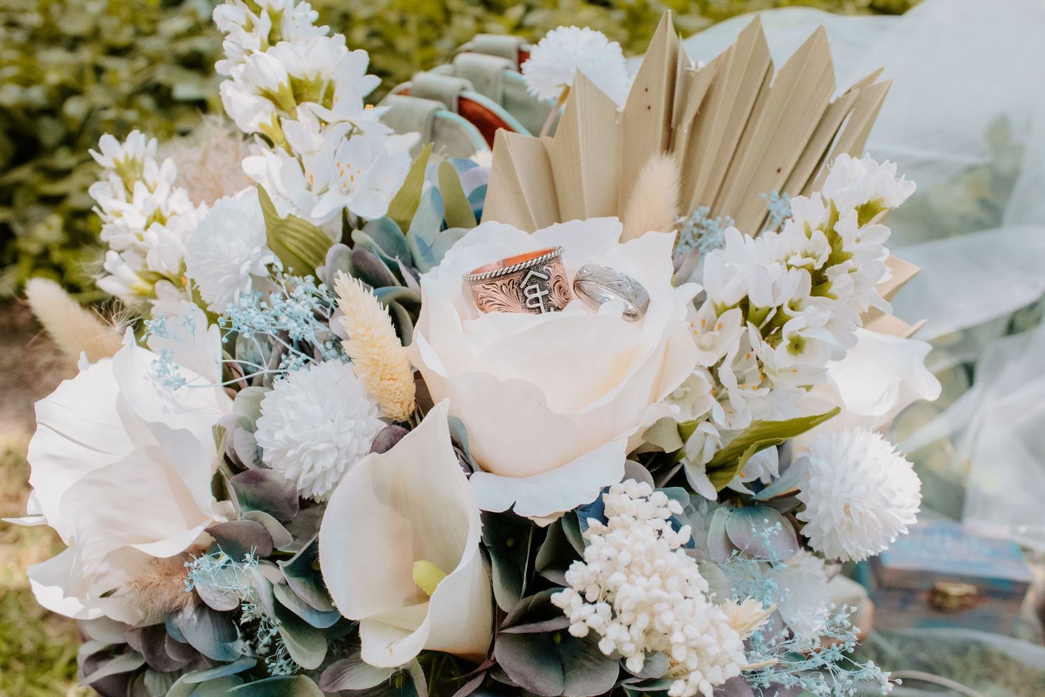 Elegant bridal bouquet with blush roses, white calla lilies, and wedding rings nestled among soft blue and cream blooms.