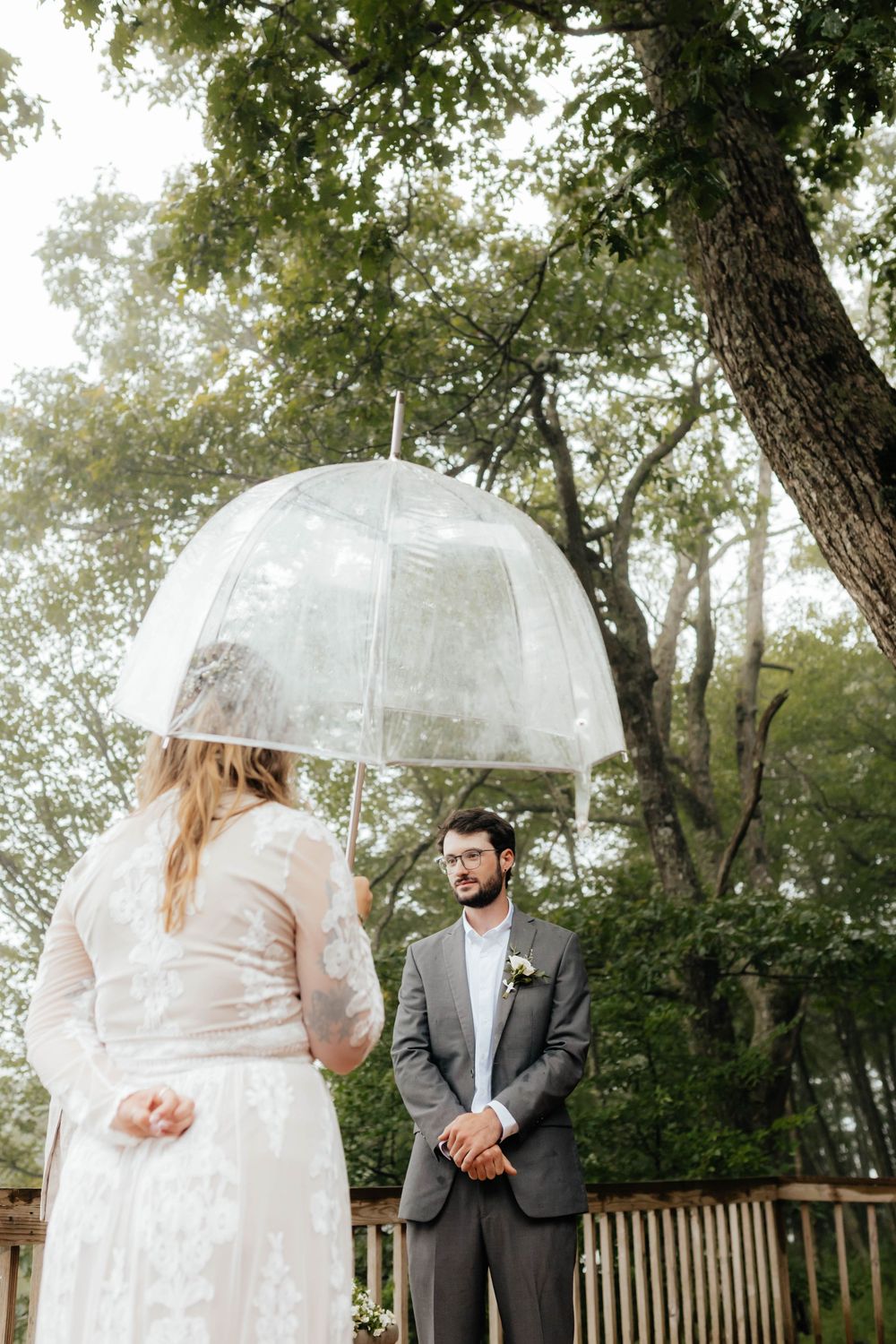 A couple shares an intimate moment under clear umbrellas in a lush garden setting on their wedding day.