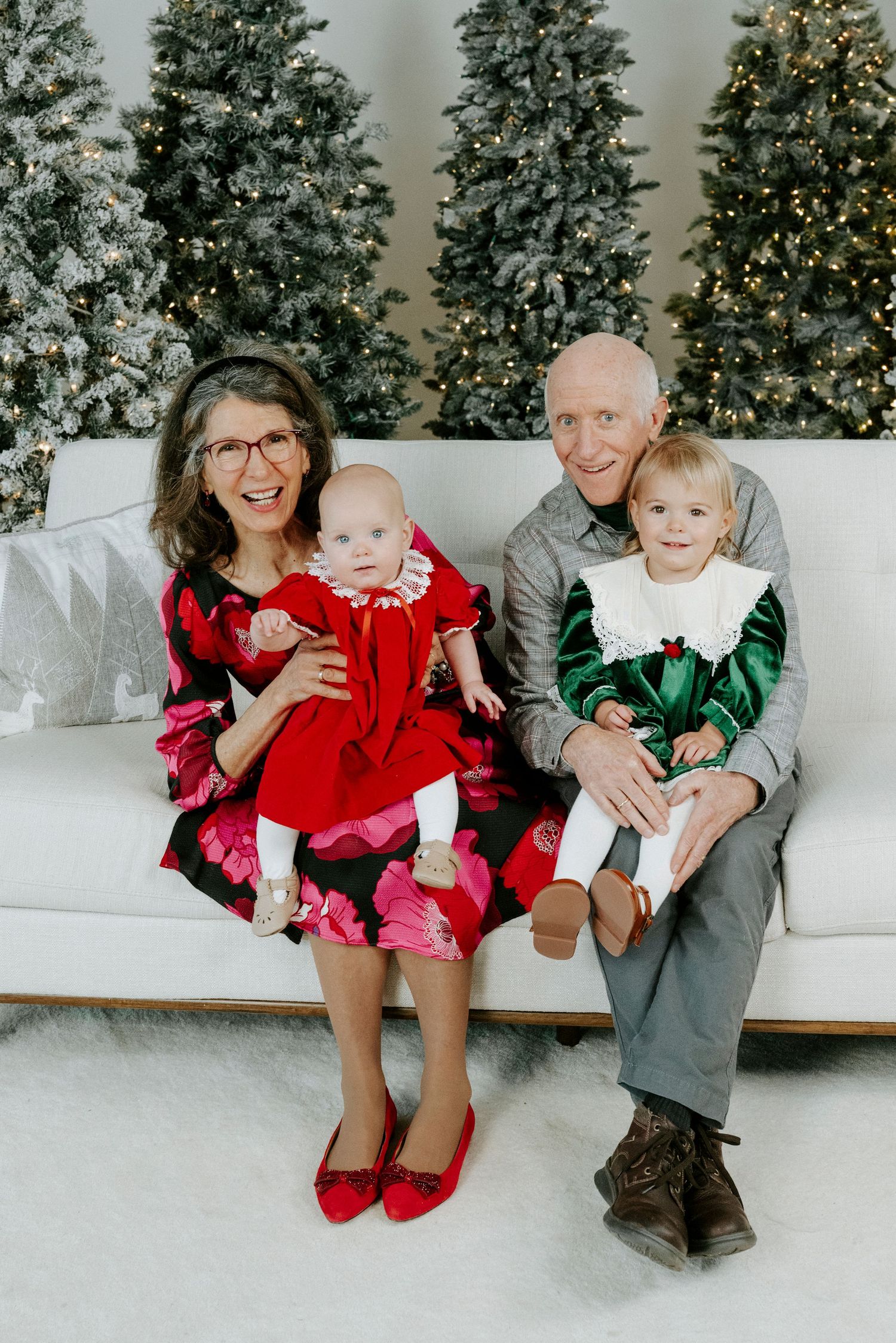 A family sits together on a white couch with decorated Christmas trees in the background.