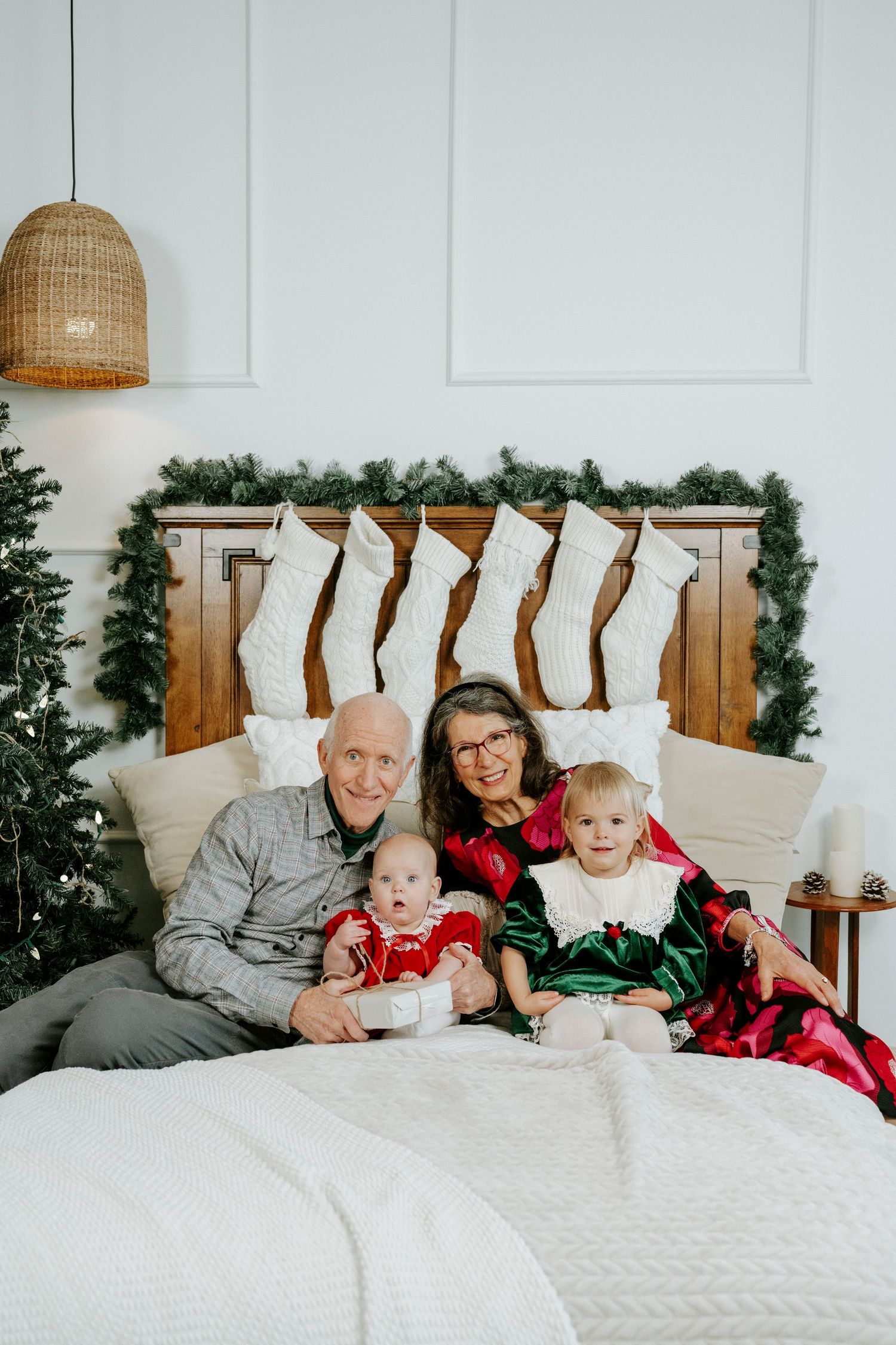 A group lounges together on a white bed with holiday decor and rattan pendant lights visible in the background.