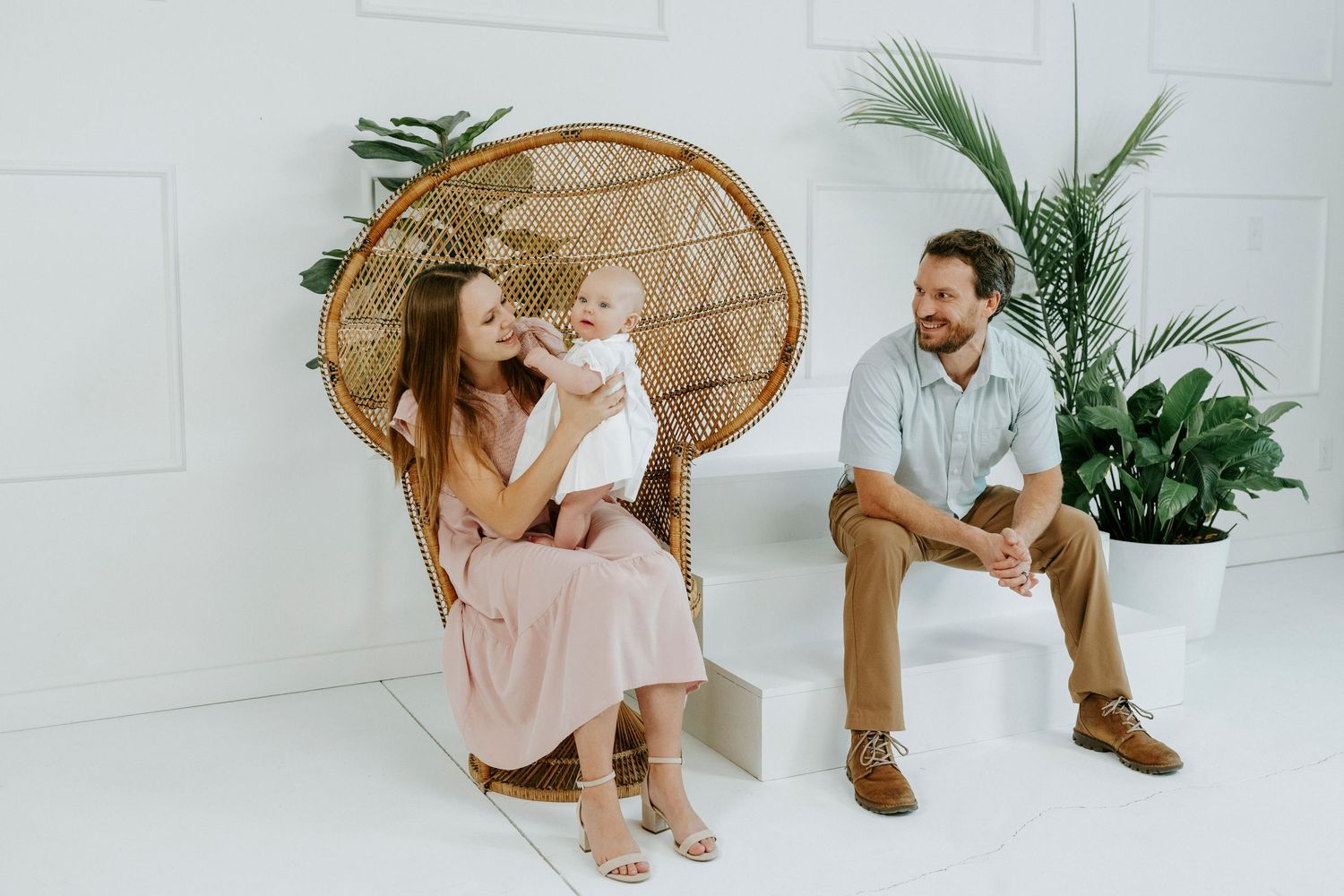 A series of romantic engagement photos in a bright white studio with wicker chairs and tropical plants.