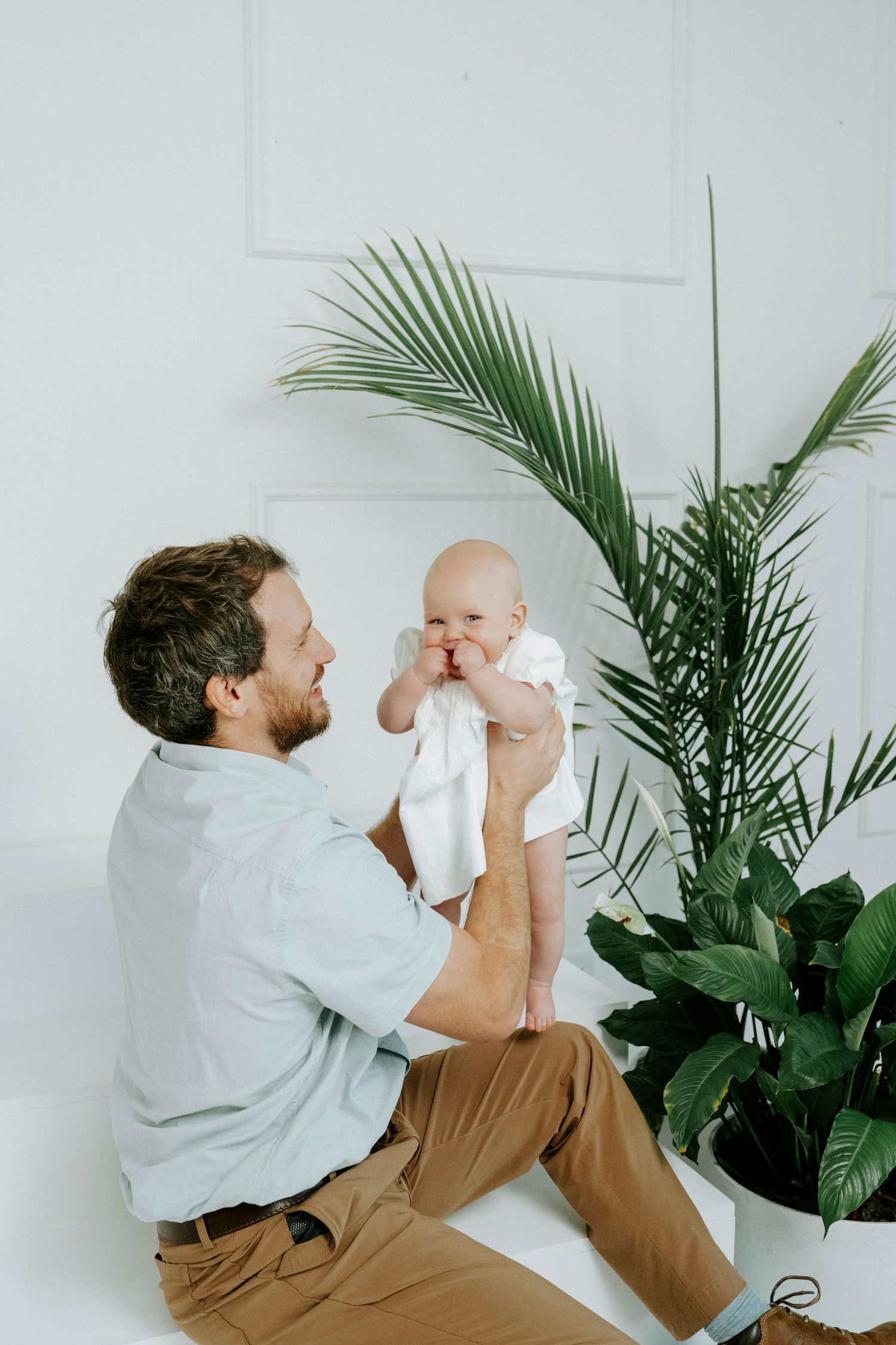 A tender moment between parent and baby against white walls with tropical plants in the background.
