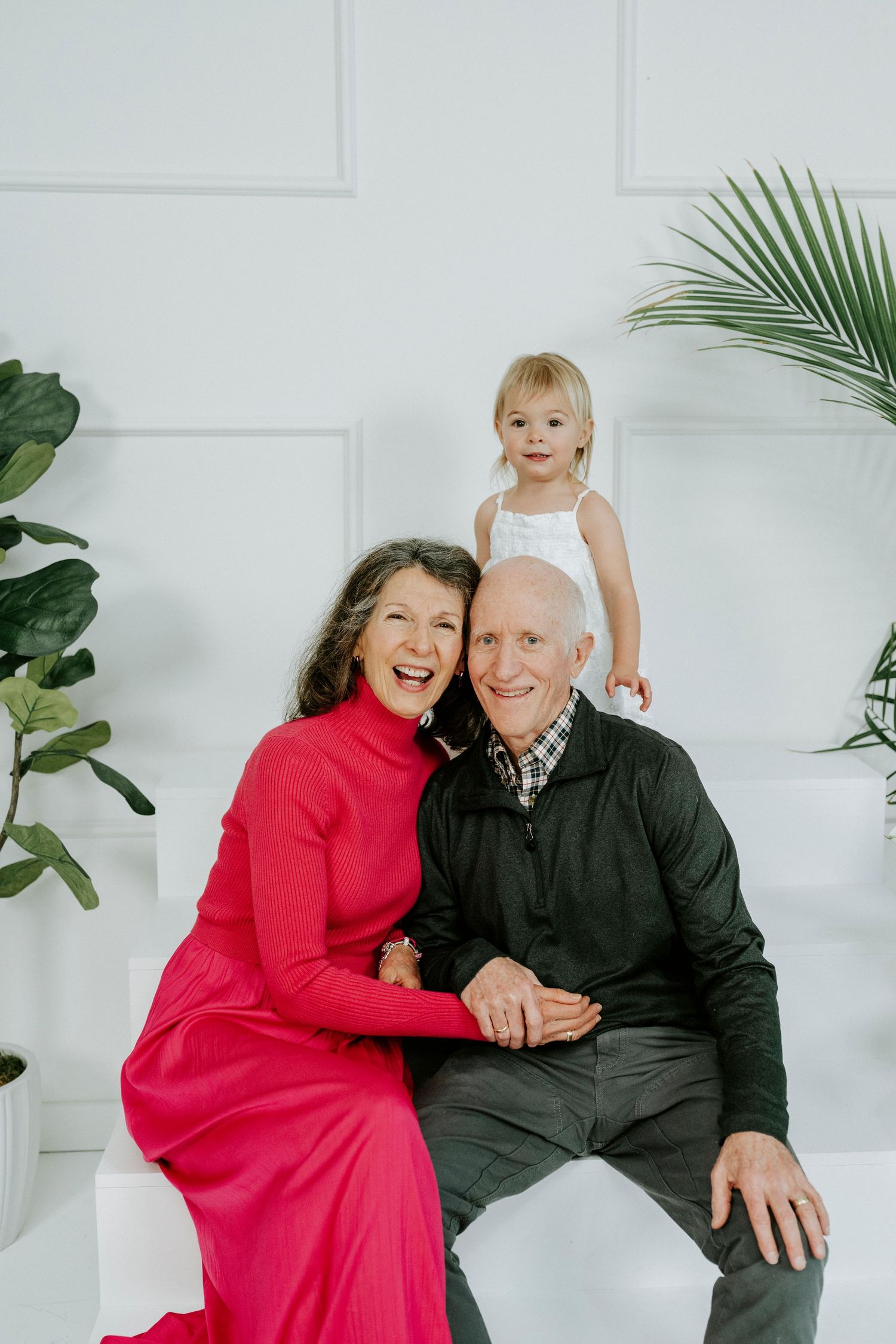 A family portrait with tropical plants and white backdrop showing three generations together.