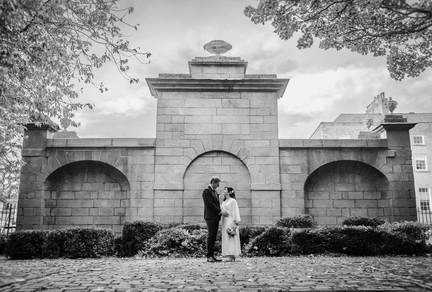 A black and white panoramic view of historic stone entrance gates with arched openings along a wall.