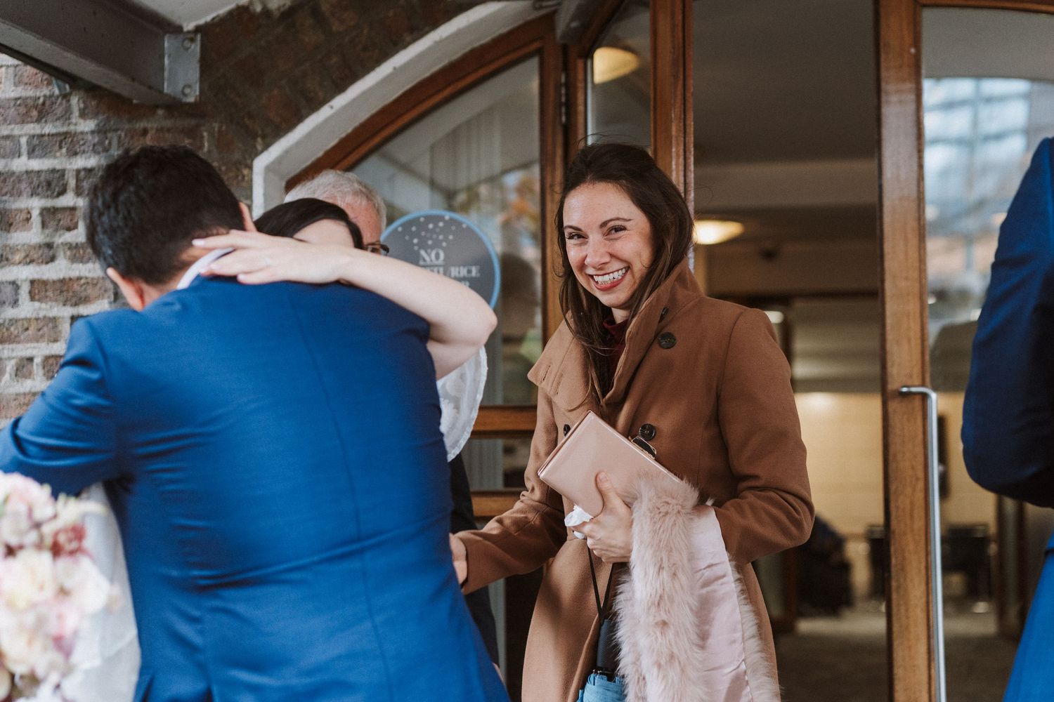 A joyful gathering of people in a doorway, with someone wearing a brown coat laughing during a casual interaction.