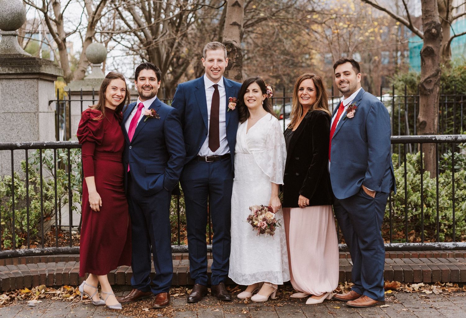 A group in formal attire poses together outdoors during an autumn wedding celebration.