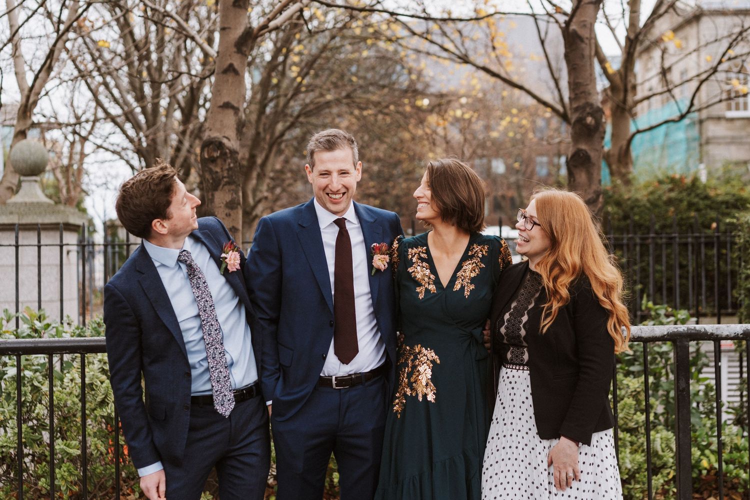 Group in formal attire stands together outdoors in front of iron fence during spring gathering.