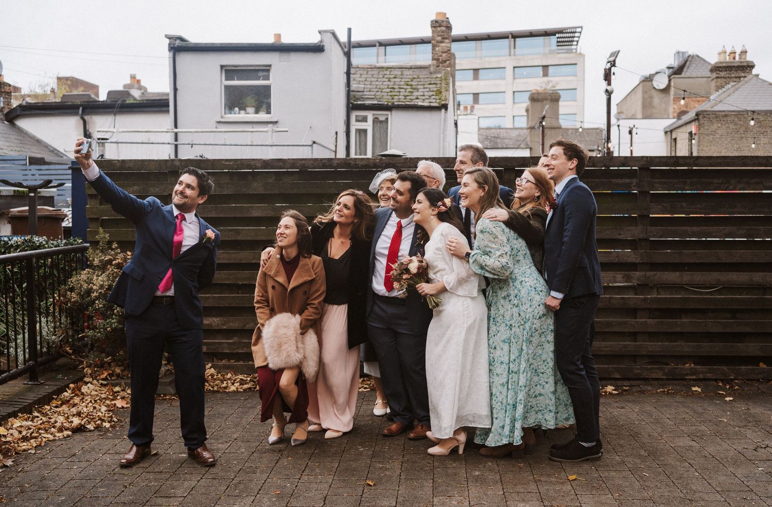 Wedding party members gather on wooden steps outdoors during a celebration.