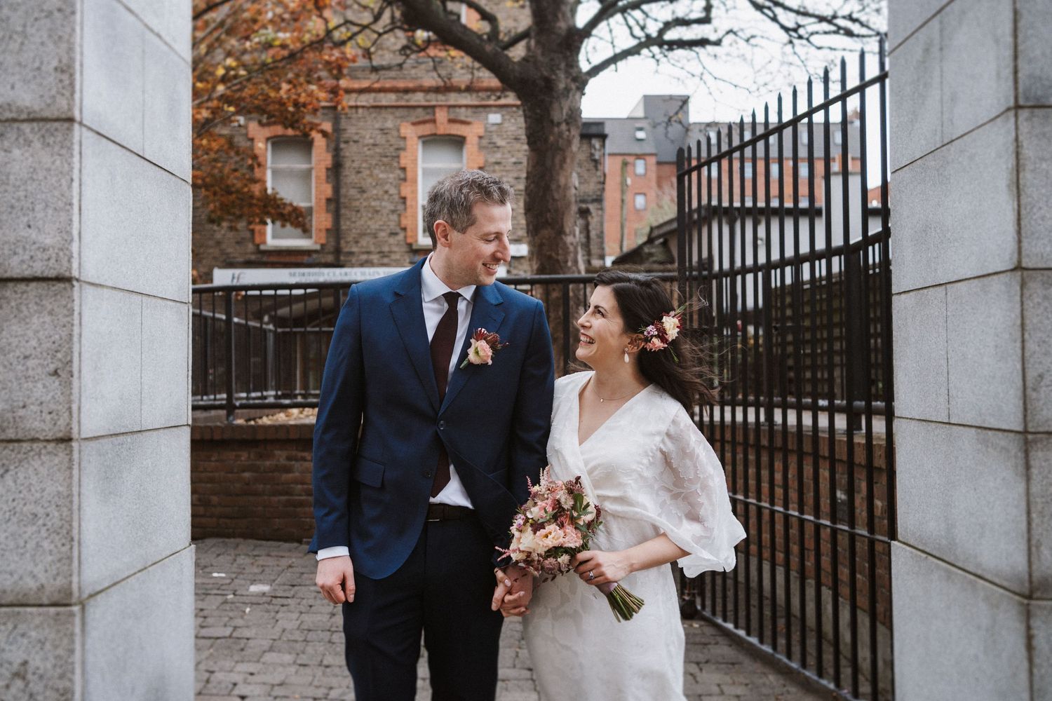 A bride and groom share a joyful moment together by iron gates on their autumn wedding day.