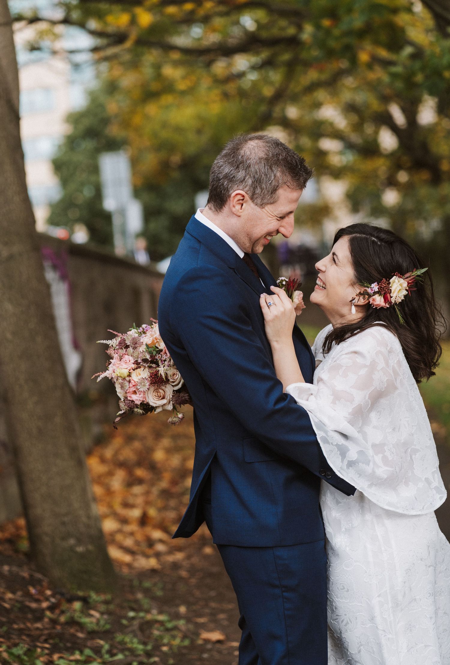 Romantic autumn wedding scene with couple embracing under trees with golden fall foliage.