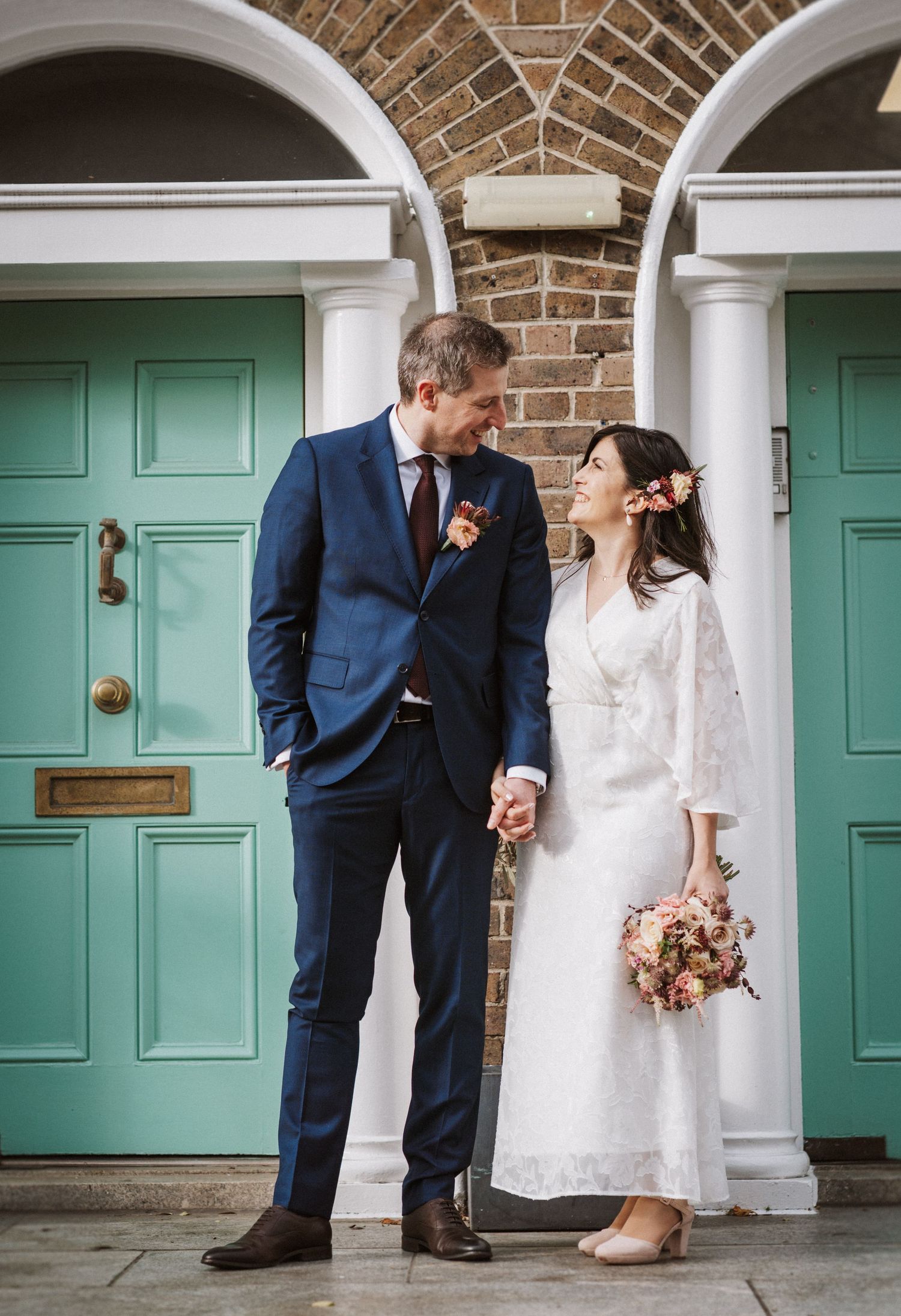 A couple in wedding attire poses in front of turquoise doors and brick walls, creating a romantic atmosphere.